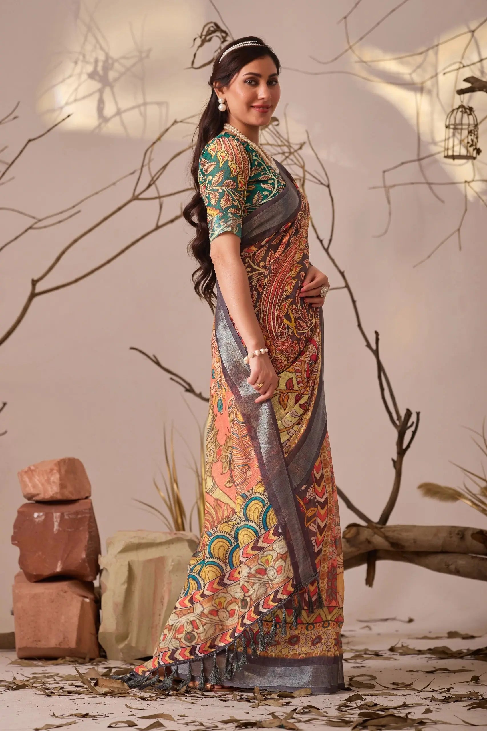 Woman in a colorful traditional outfit standing in a rustic setting with branches and stones.
